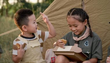 Two Asian kids (a boy and a girl) eating beside a camping tent