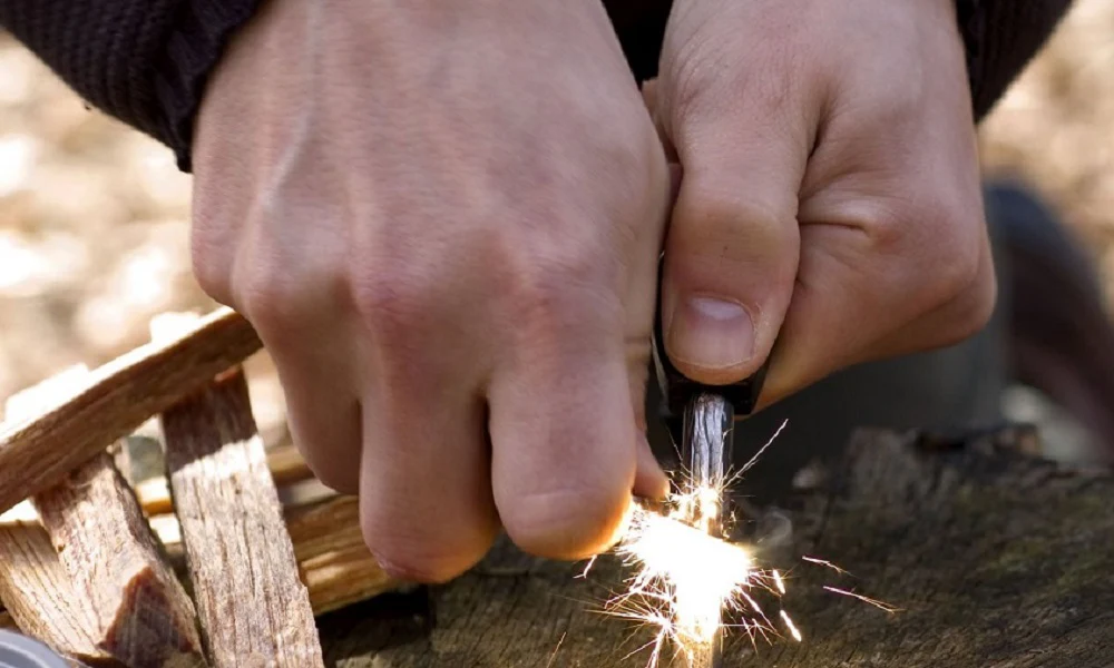 A camper gathers some grasses and wood, lighting it up with a flint and steel method as a technique on  how to start a fire without matches or lighters