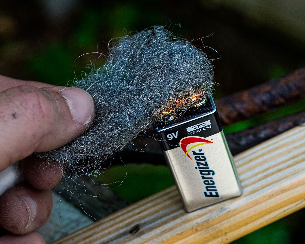 Someone using a battery and steel wool to light fire as a technique on  how to start a fire without matches or lighters